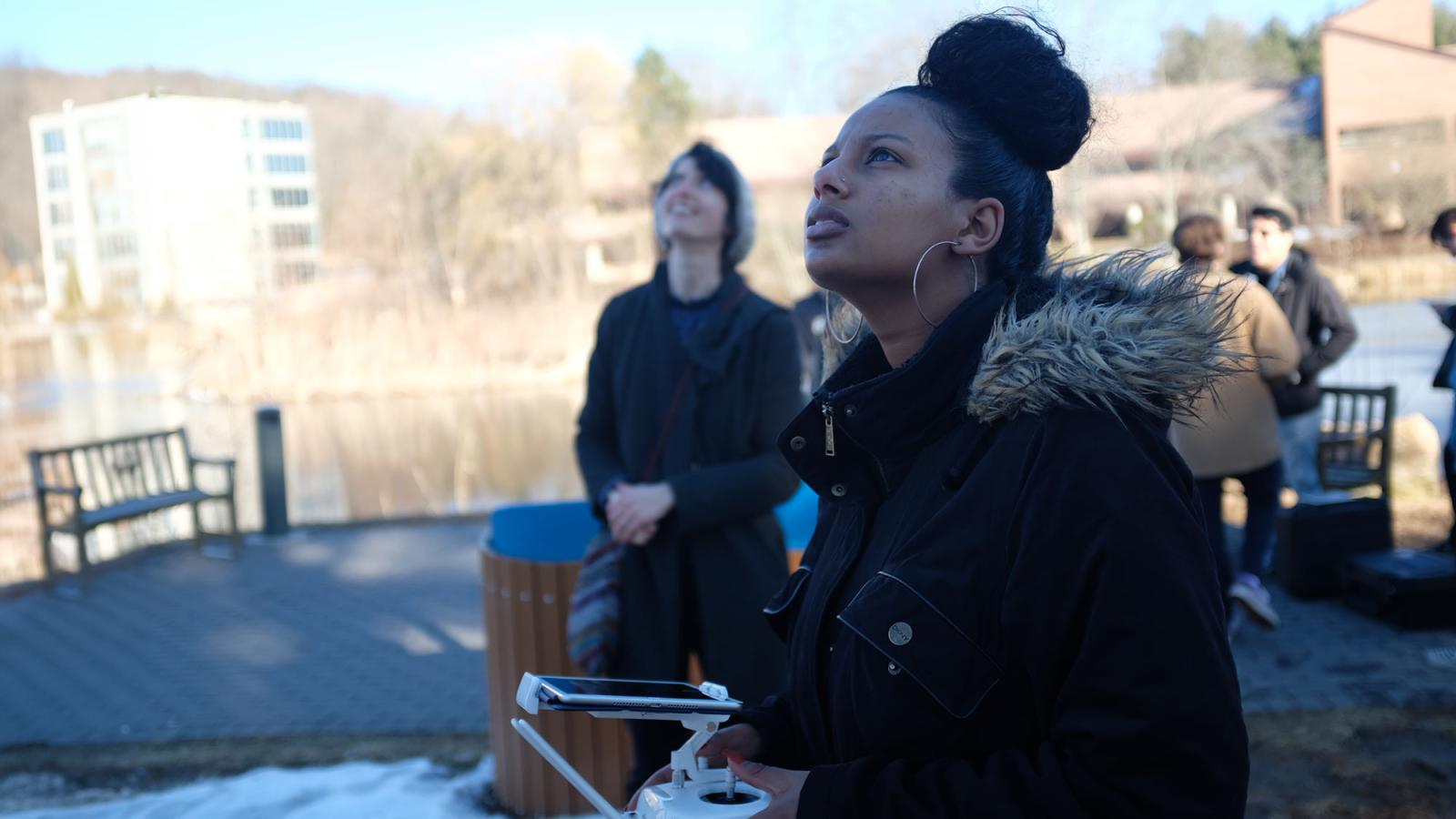 Pace University's Media, Communications, and Visual Arts student holding controller and looking up at flying drone