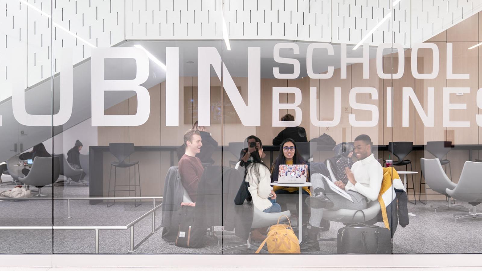 group of students sitting and studying in One Pace Plaza behind glass wall with Lubin School of Business sign
