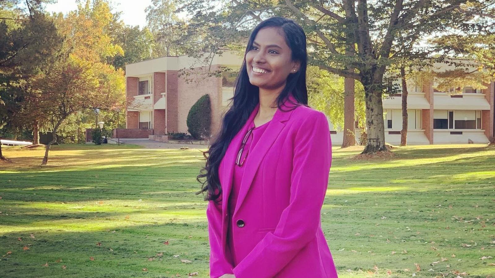 Lubin student Akshata Swami '24 standing outside on a lawn near trees and campus building