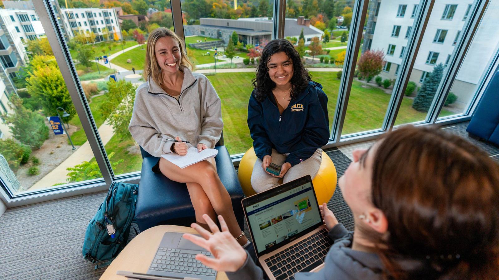 group of Pace University students sitting in the lounge on our Pleasantville Campus overlooking the bright green Alumni Hall quad. 