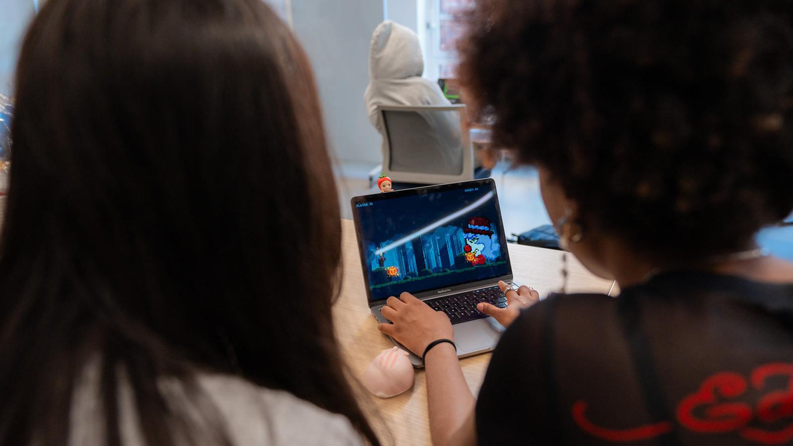Two Pace University students sit at a laptop playing through a video game