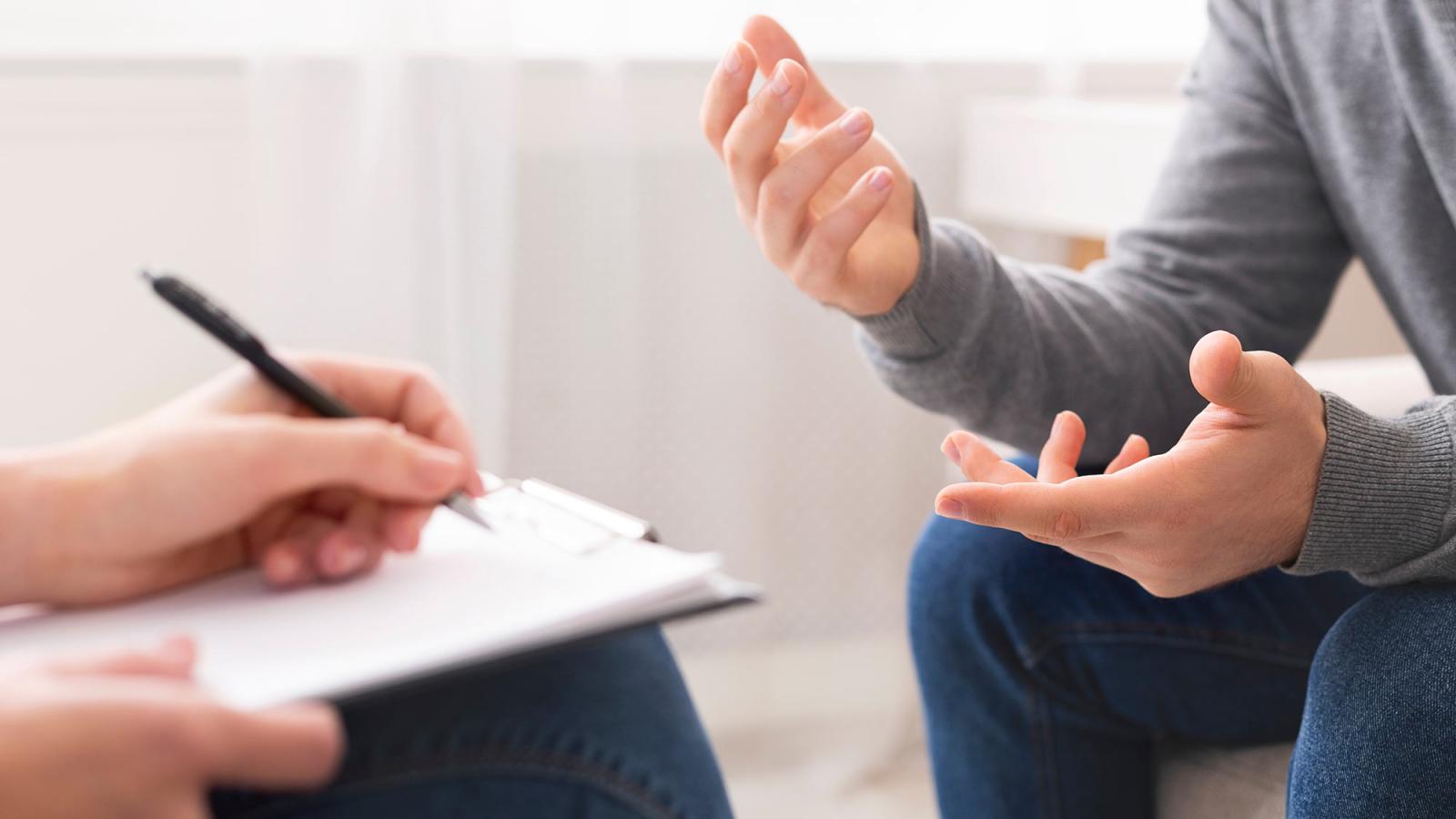 two people sitting across from each other, the person on the left is writing on a notepad