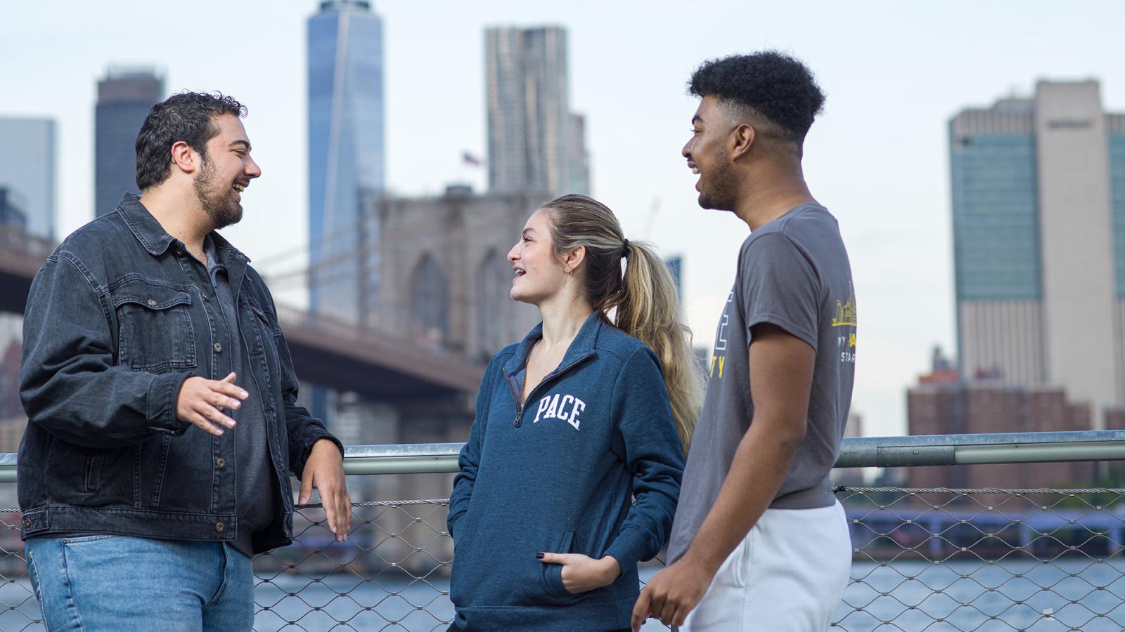 Three Pace University students speaking with the NYC skyline in the background.