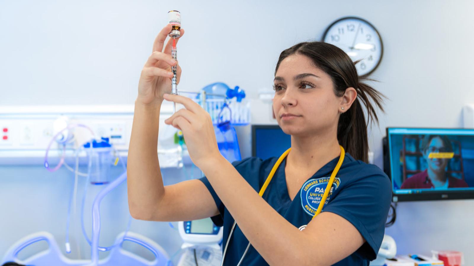 A Pace University nursing student in a simulation lab drawing liquid into a syringe.