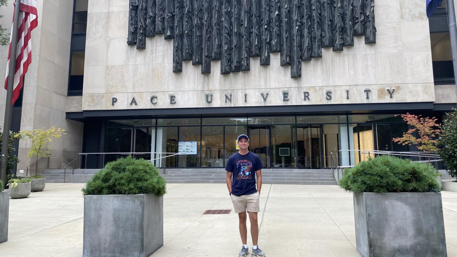 Will Schmid posing in front of One Pace Plaza on the Pace University New York City campus.