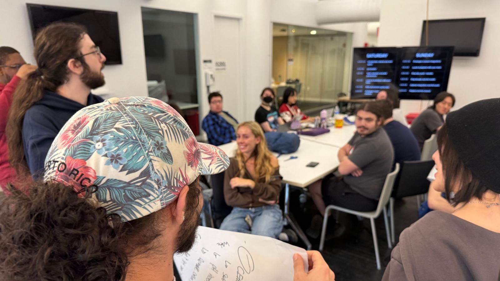 A group of Seidenberg students talking to a group of Parsons students while sitting around a table at the "Phenomenal" game jam.