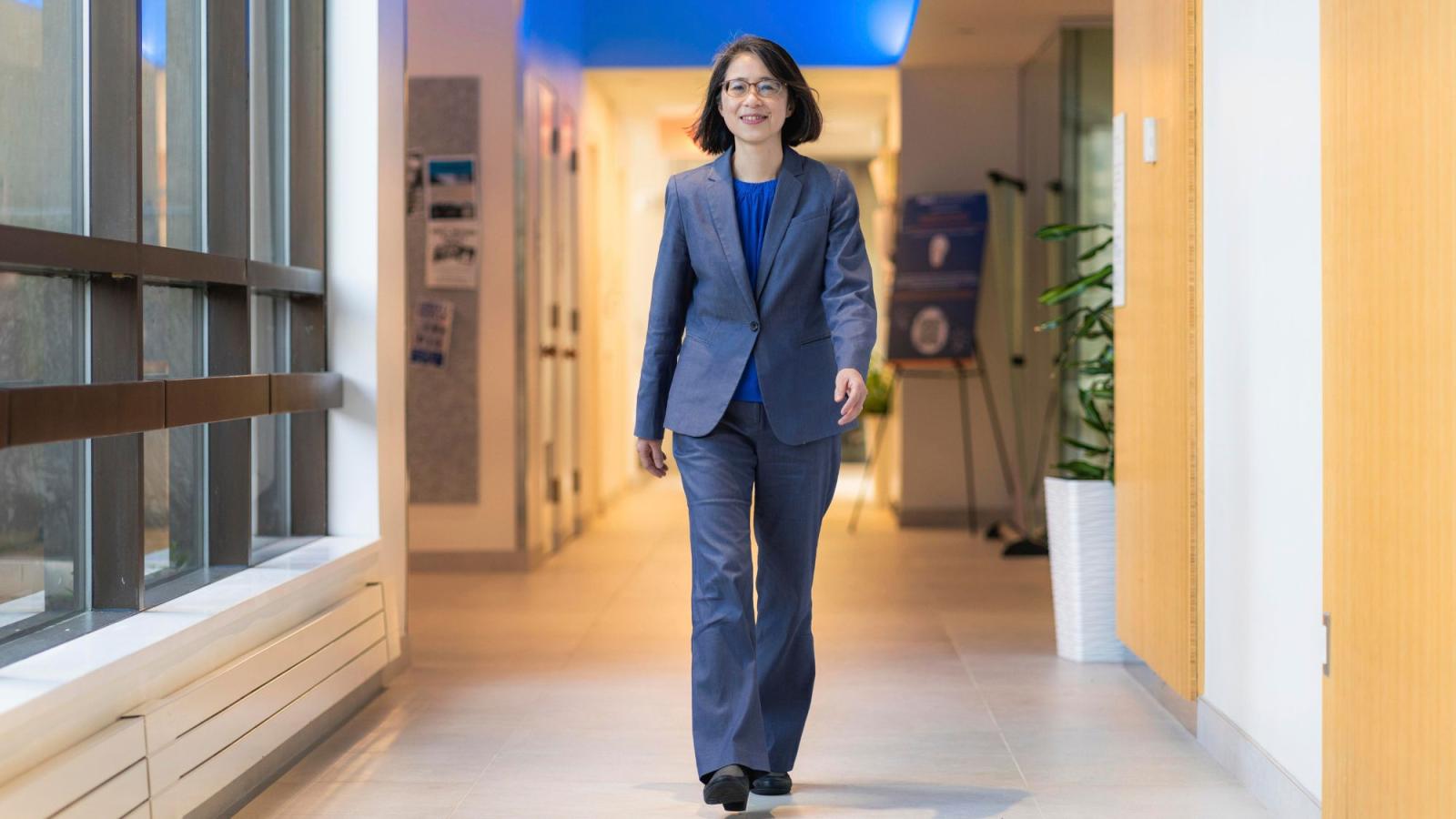 Interim Dean Li-Chiou Chen of Pace University's Seidenberg School of CSIS walking through a hallway while wearing a suit at Pace University's One Pace Plaza building.