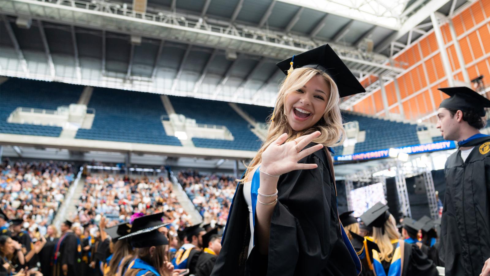 A graduate waving to the camera at Pace University's commencement ceremony.