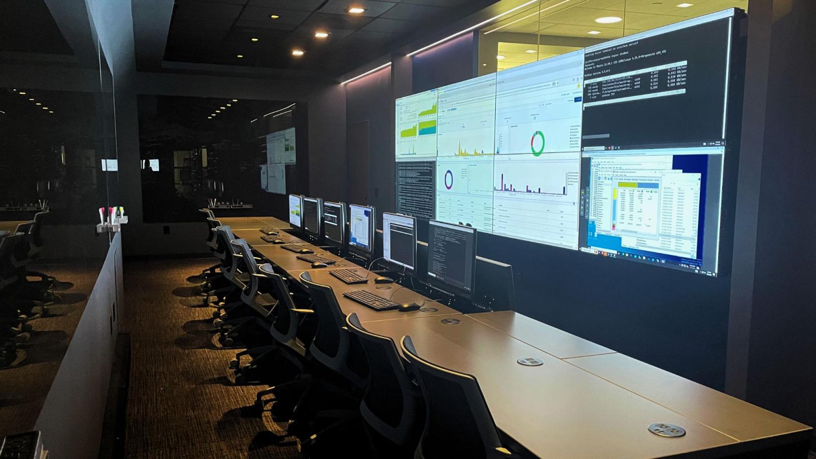 Image showing the layout of the Pace Cyber Range - a long desk with computers and chairs placed in front of a giant wall of screens.