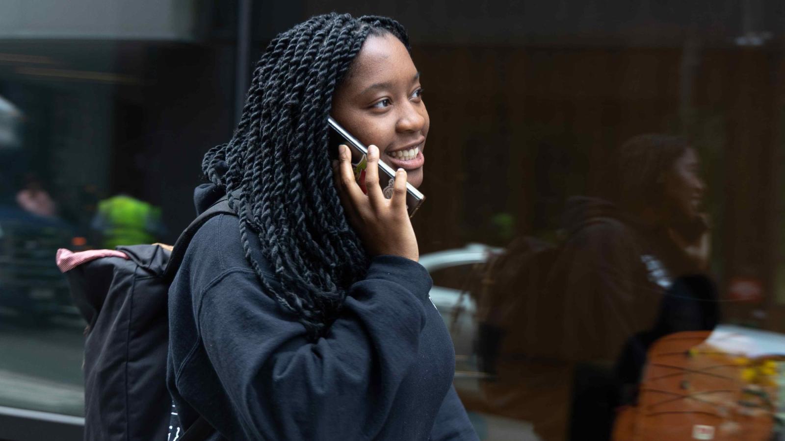 Seidenberg student walking on the street while talking on the phone.
