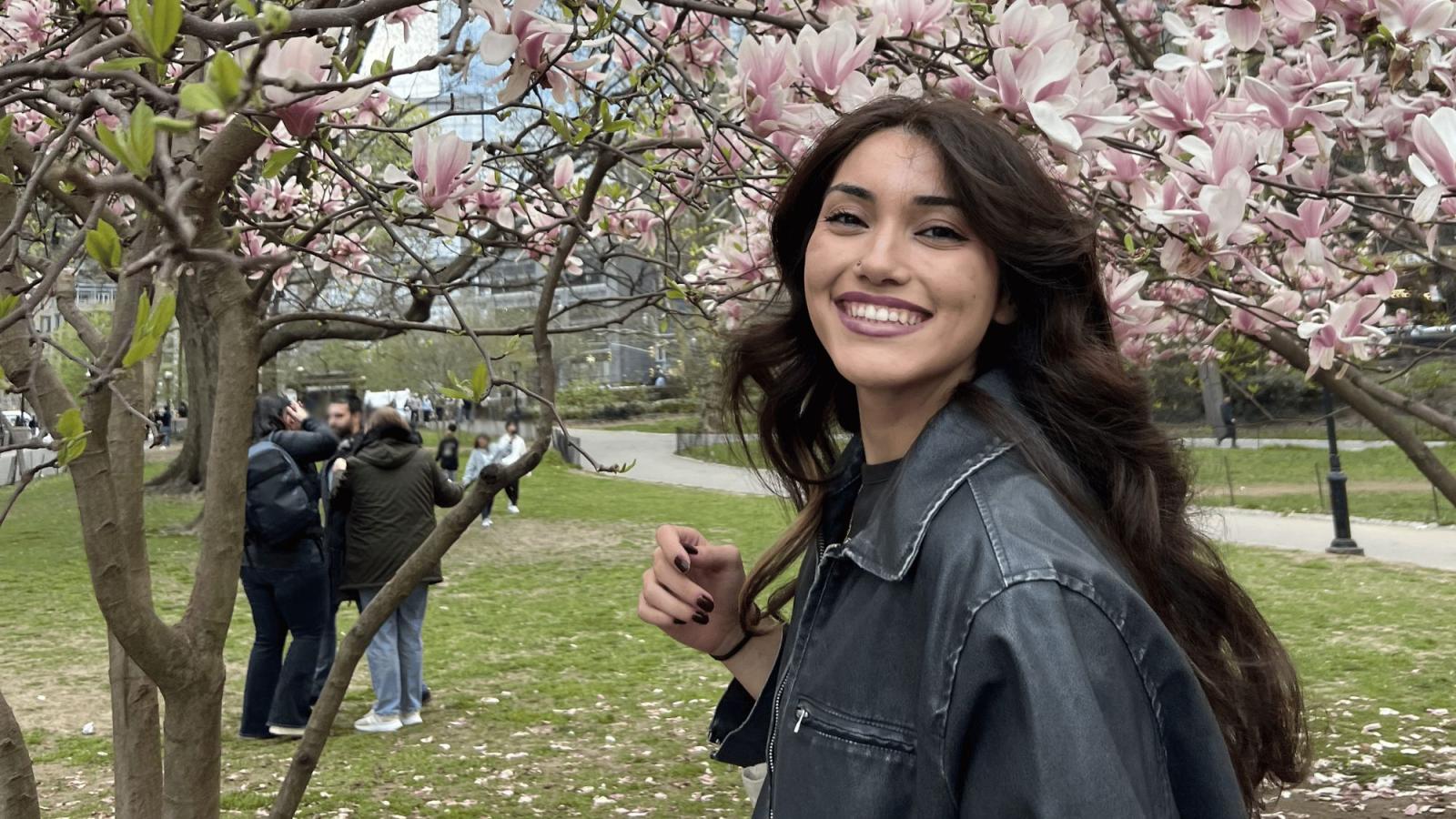 Seidenberg student Daisy Molina posing for a photo in front of cherry blossom trees.