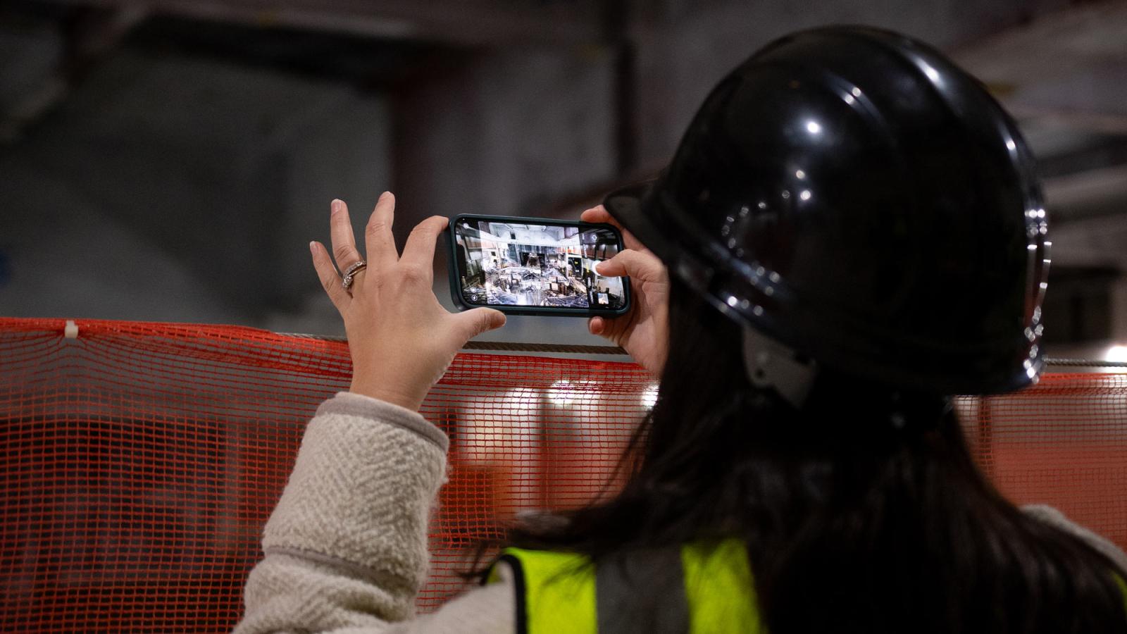 Woman wearing a hardhat and taking a photo of the construction of One Pace Plaza East.