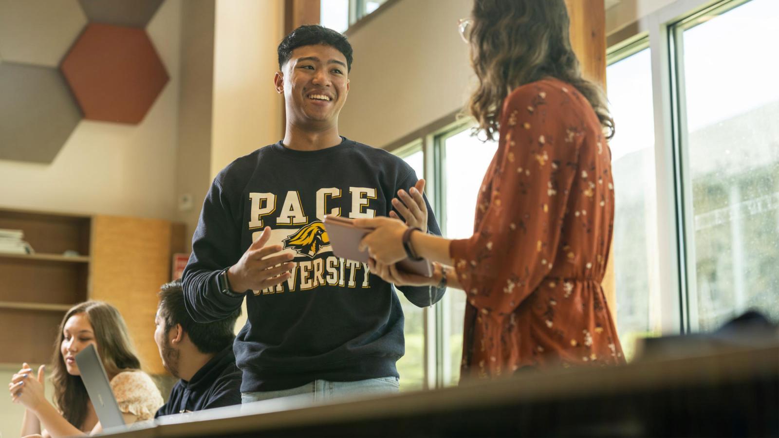 A student in a classroom talking with a professor.