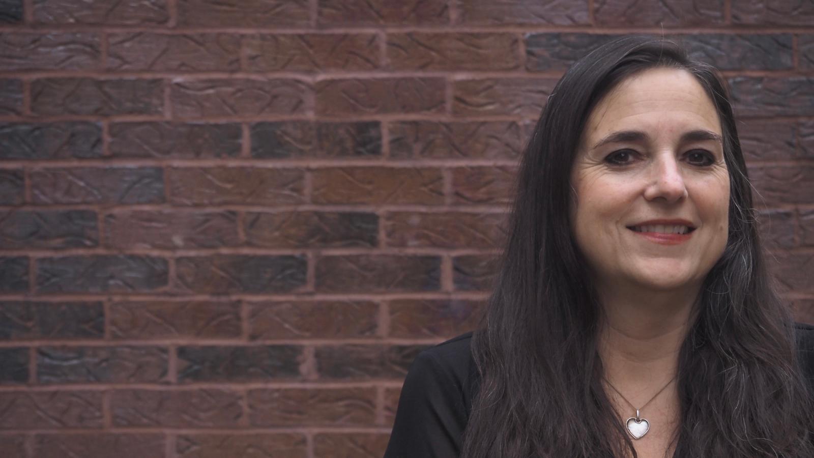 Pace University faculty Jessica Magaldi stands in front of a brick wall