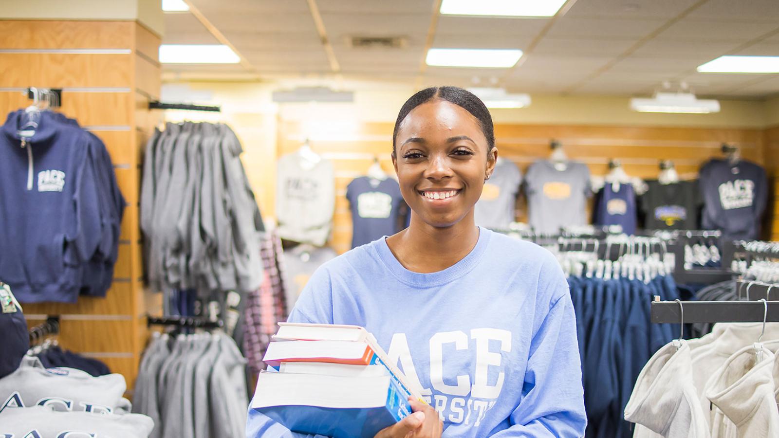 Pace University female student holding a stack of books while standing in the bookstore.