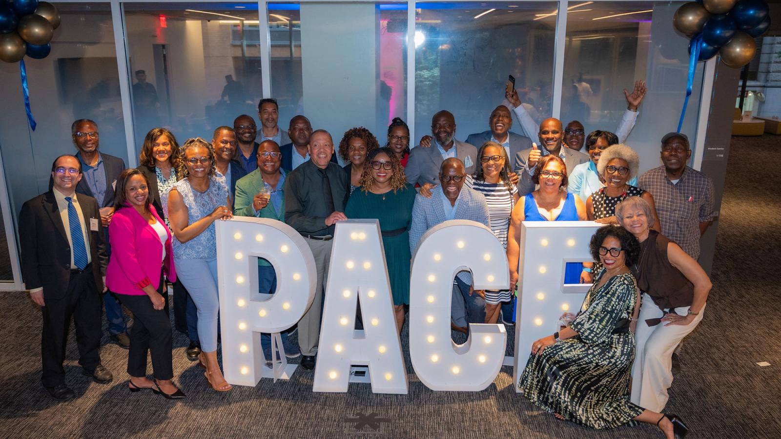 Group of Pace University alumni celebrating the 2025 Reunion, smiling at the camera standing next to a Pace sign.