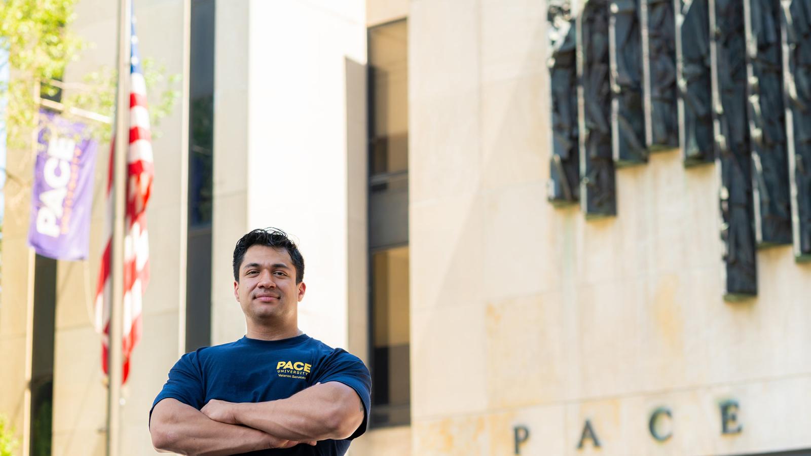 Smiling man with arms crossed in front of a Pace building and an American flag