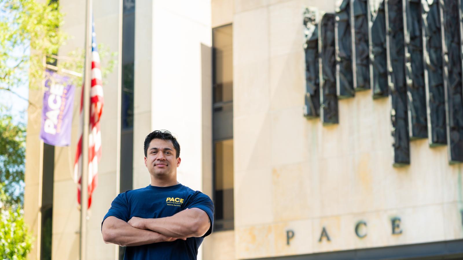 Smiling man with arms crossed in front of a Pace building and an American flag.