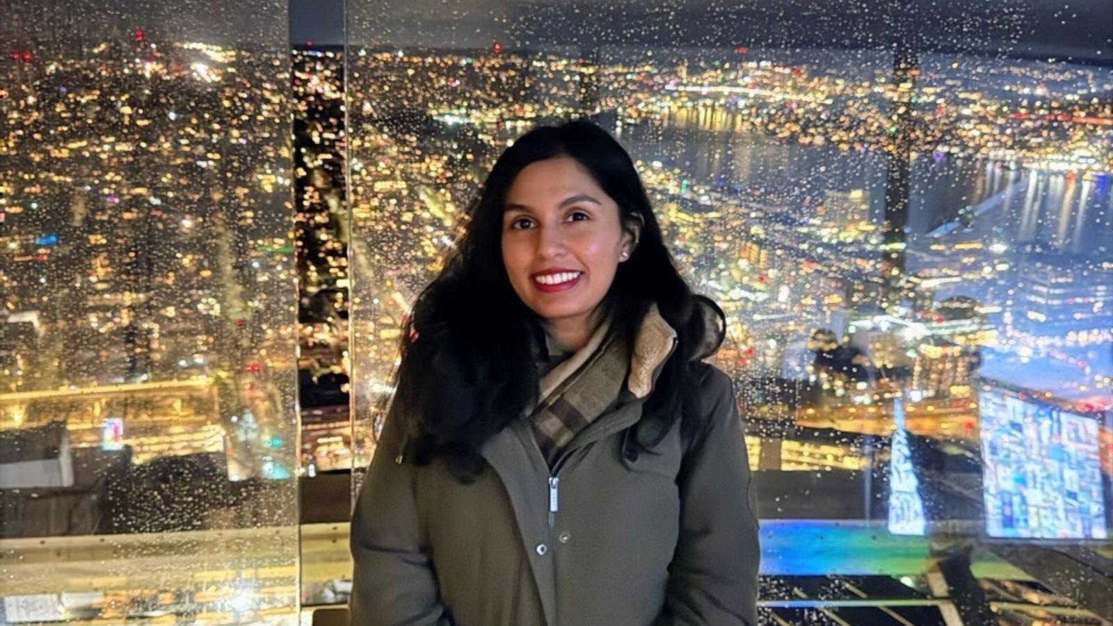 Pace Seidenberg alum Lolita Tiwari posing for a photo in front of a rainy cityscape at night.