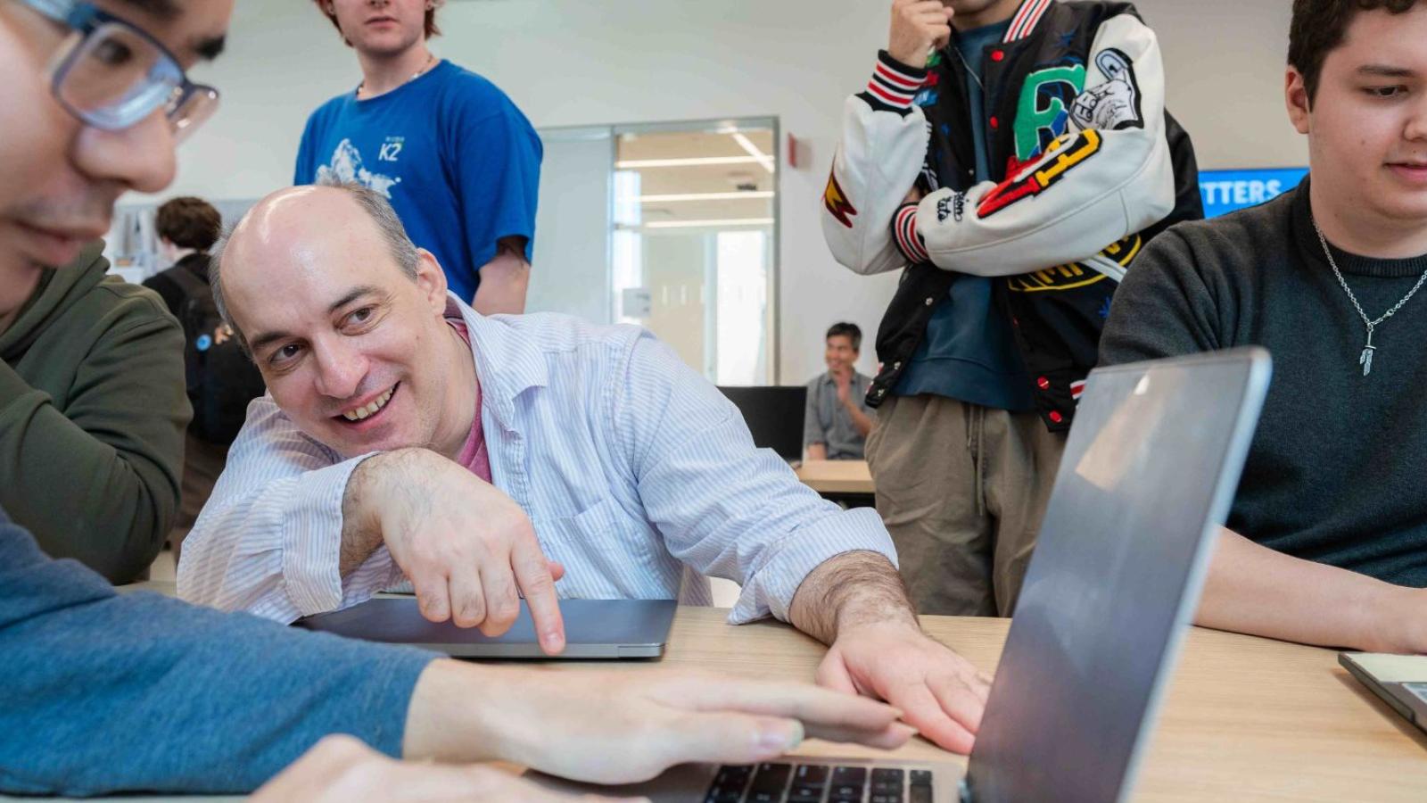 Seidenberg professor Carmine Guida working with a group of students on their laptops.