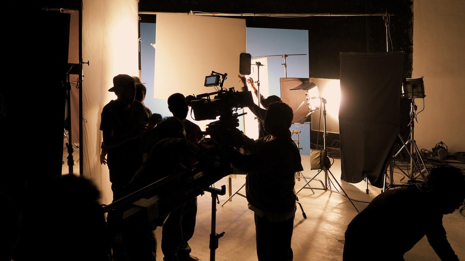 Silhouette of film crews and video camera on special dolly crane with film lights equipment and blue screen set.