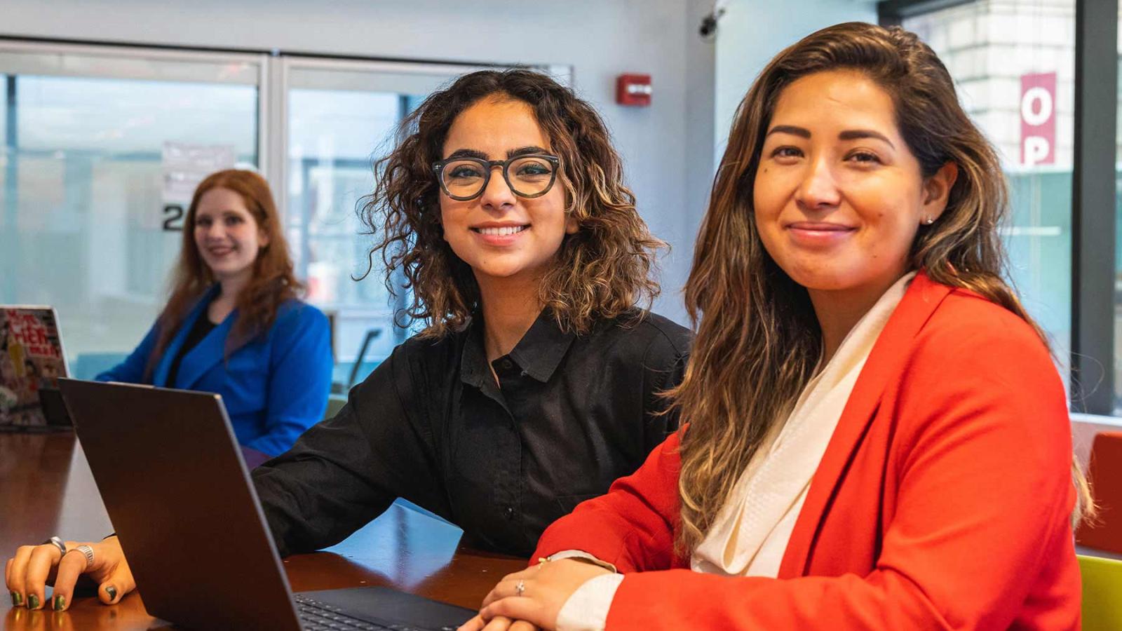 Two women sitting in front of a laptop smiling at the camera.