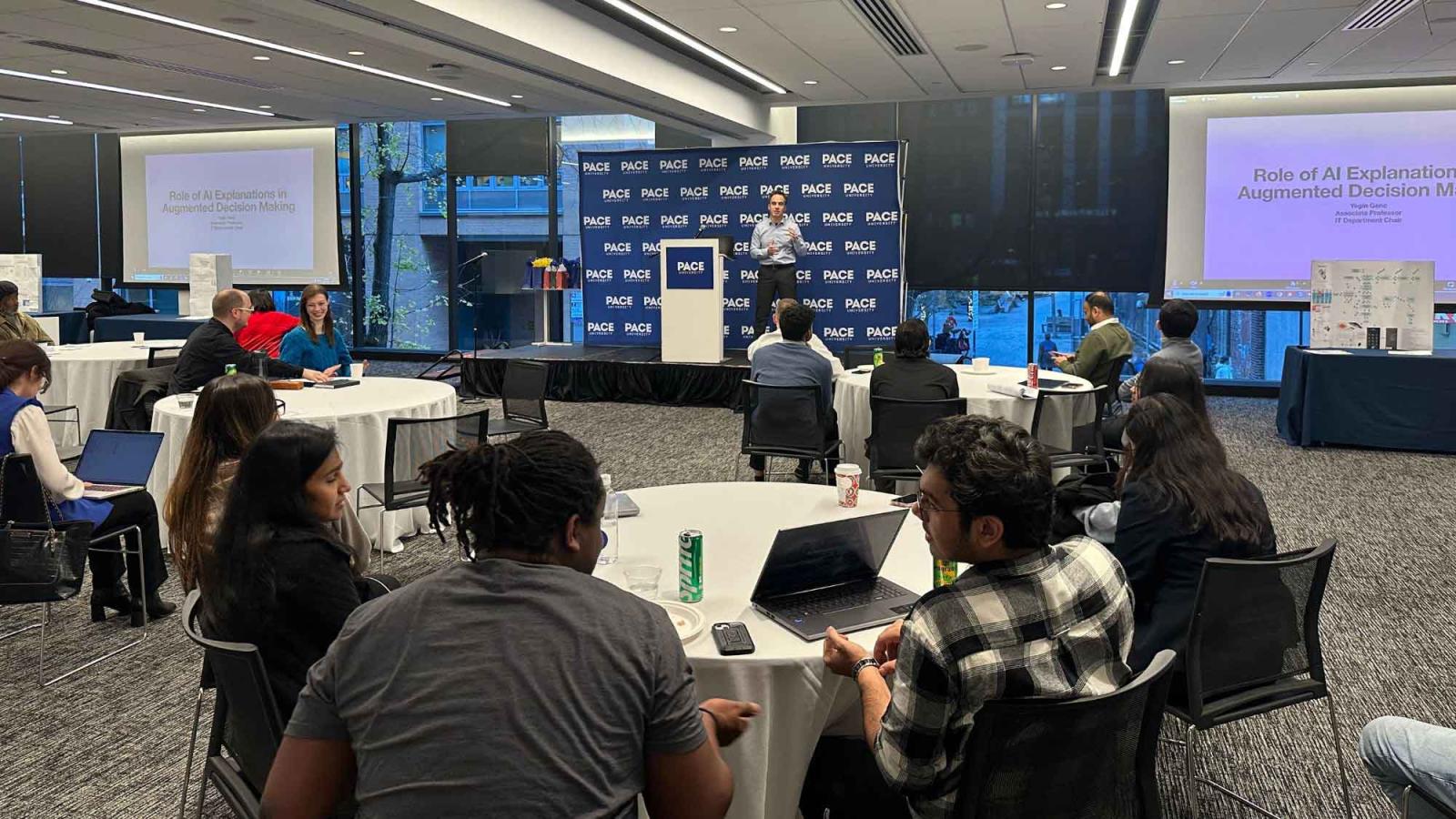 Dr. Yegin Genc, professor at Pace University's Seidenberg School of CSIS, presenting to a room full of students and faculty on a stage during the Seidenberg Annual Research Day.