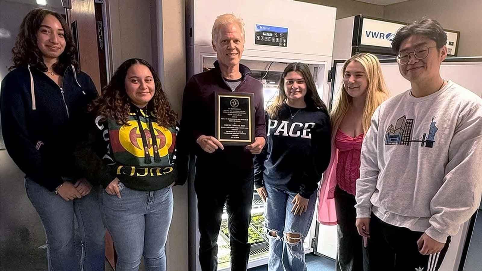 Pace University Biology Professor Eric Brenner standing with his students, holding an award