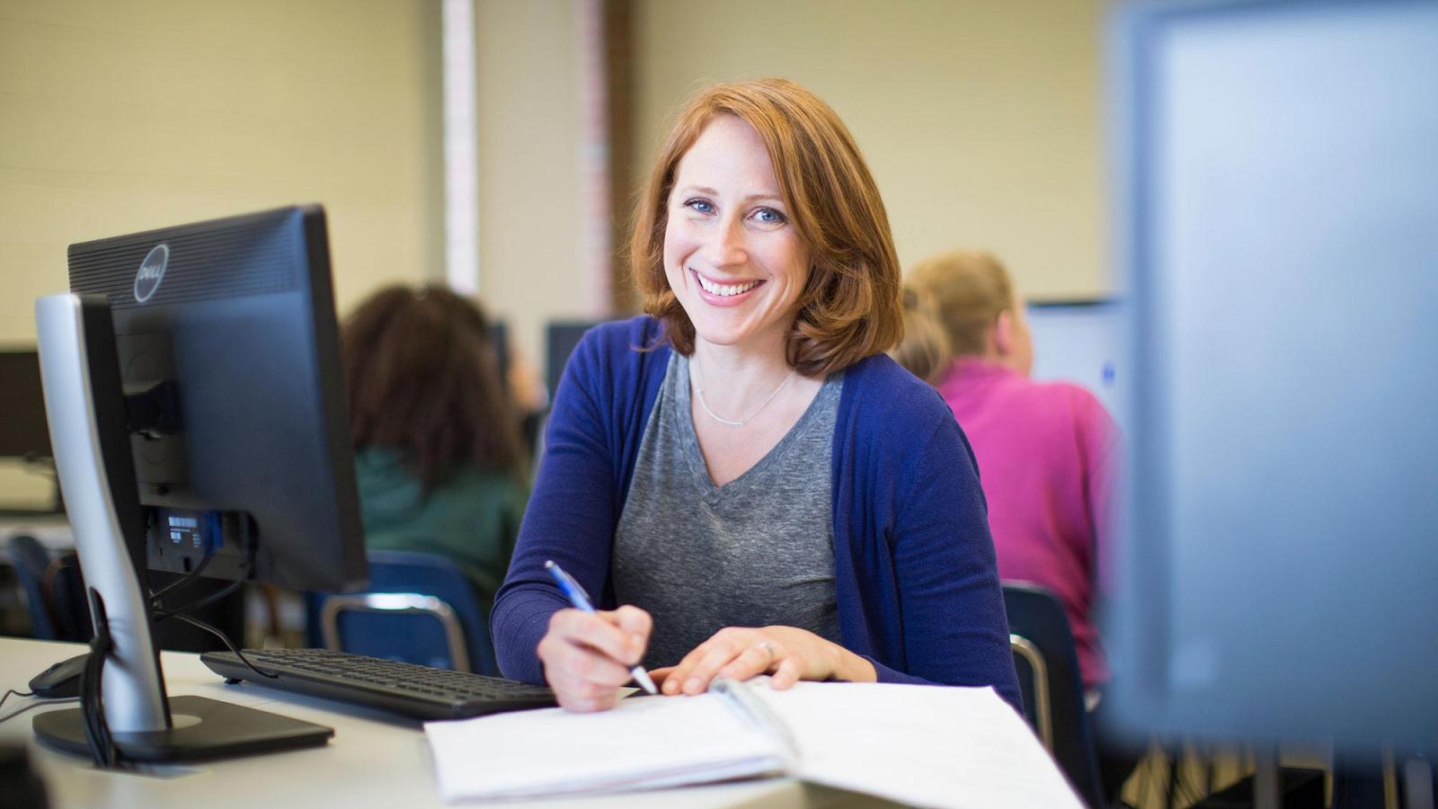 Female Pace University student, smiling at the camera, sitting behind a computer.