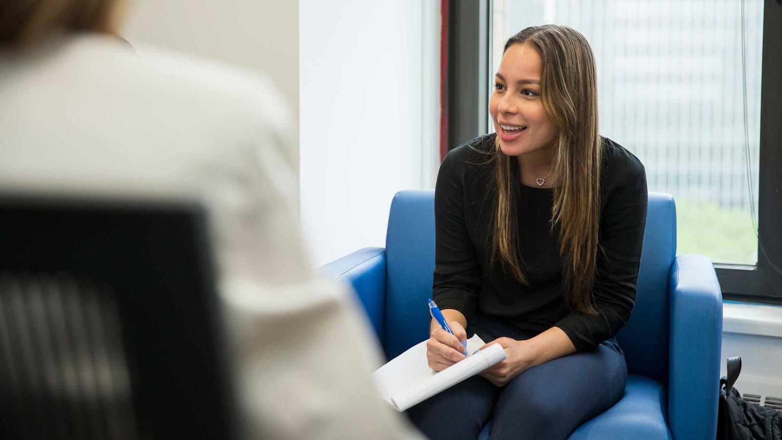 Pace University student sitting in a chair, smiling and talking.