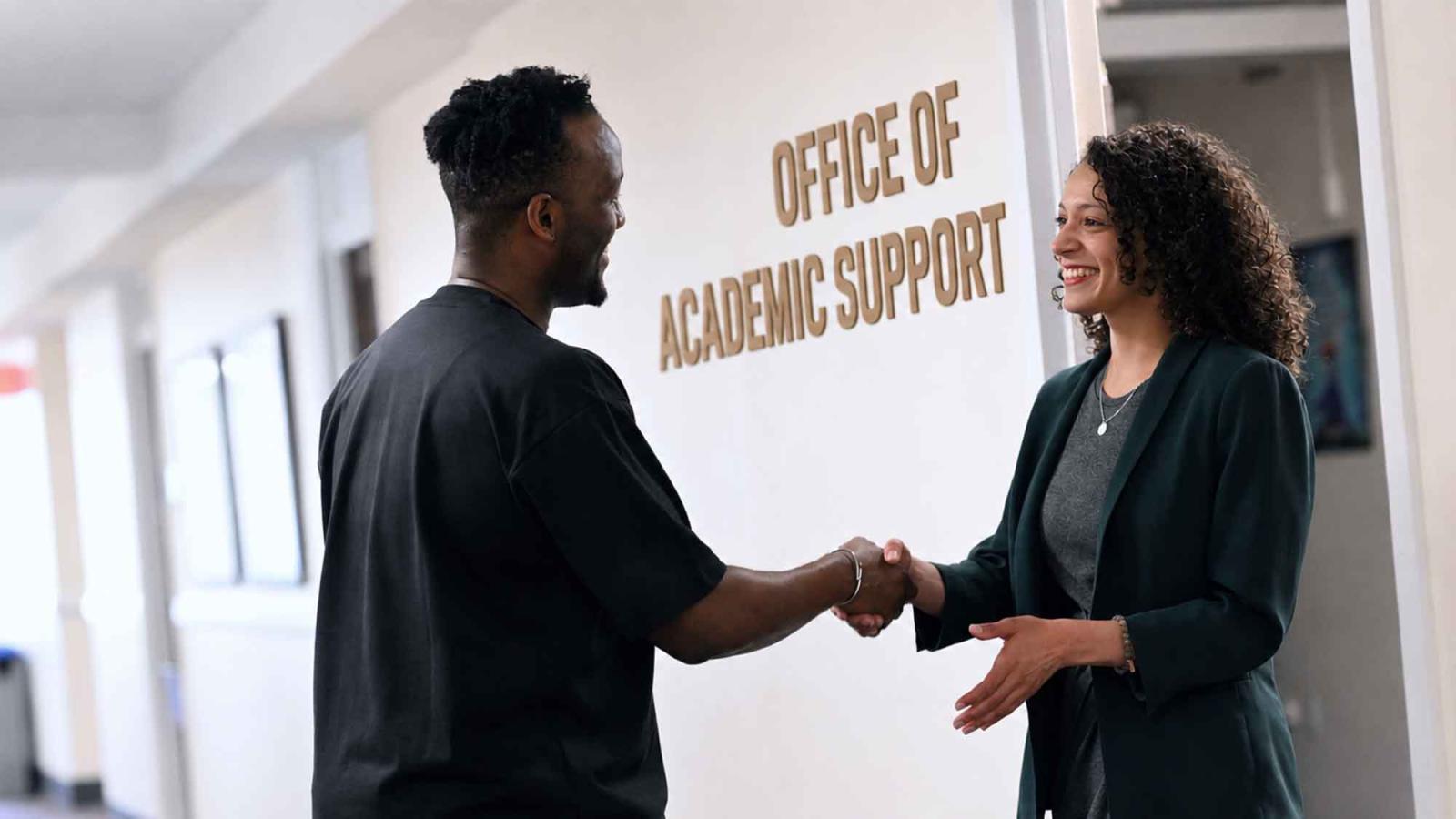 Outside the office of Office of Academic Support and Bar Performance with two people shaking hands