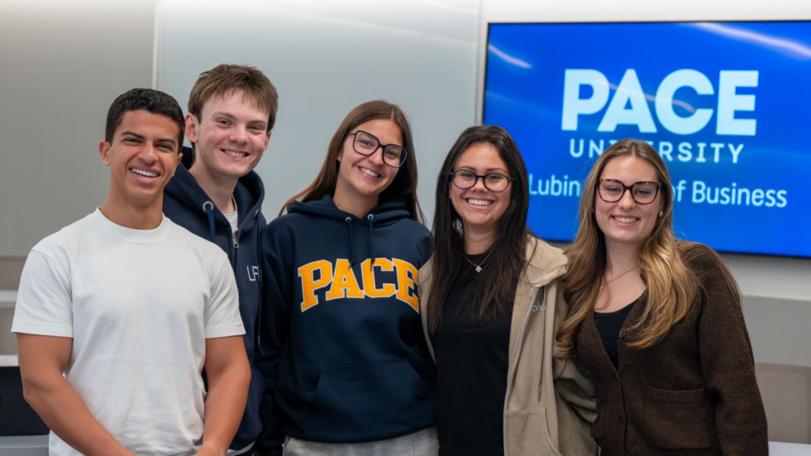 5 Pace University Lubin students posing in front of a display screen with the Lubin logo