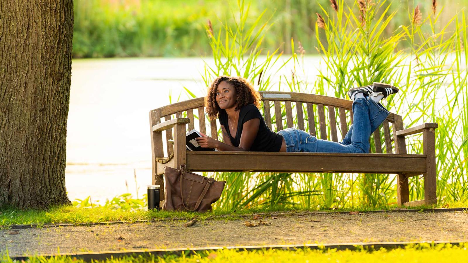 Pace University student, laying on a bench, reading a book on the Westchester Campus.