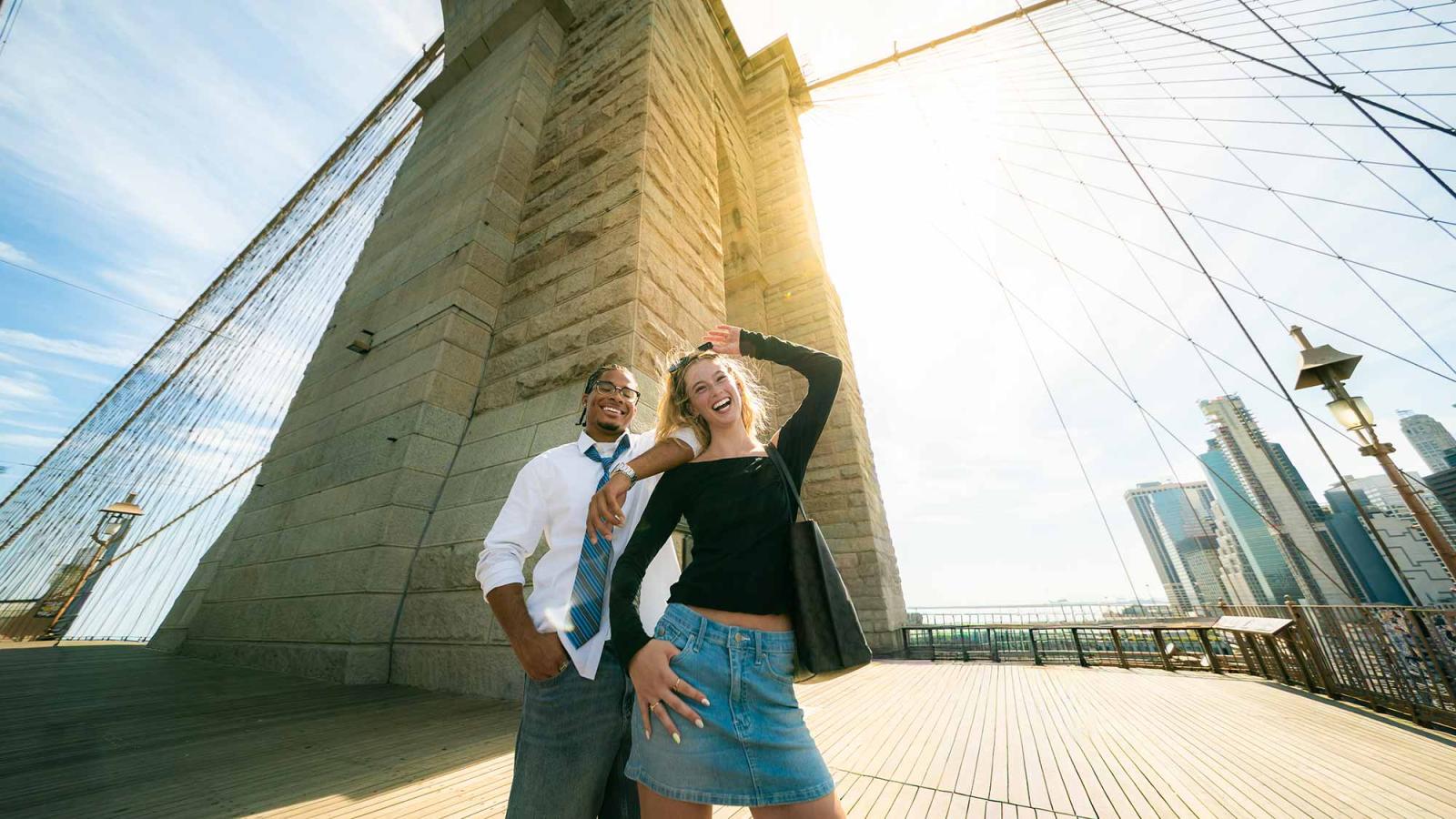 Two Pace University students standing on the Brooklyn Bridge, smiling at the camera in NYC.