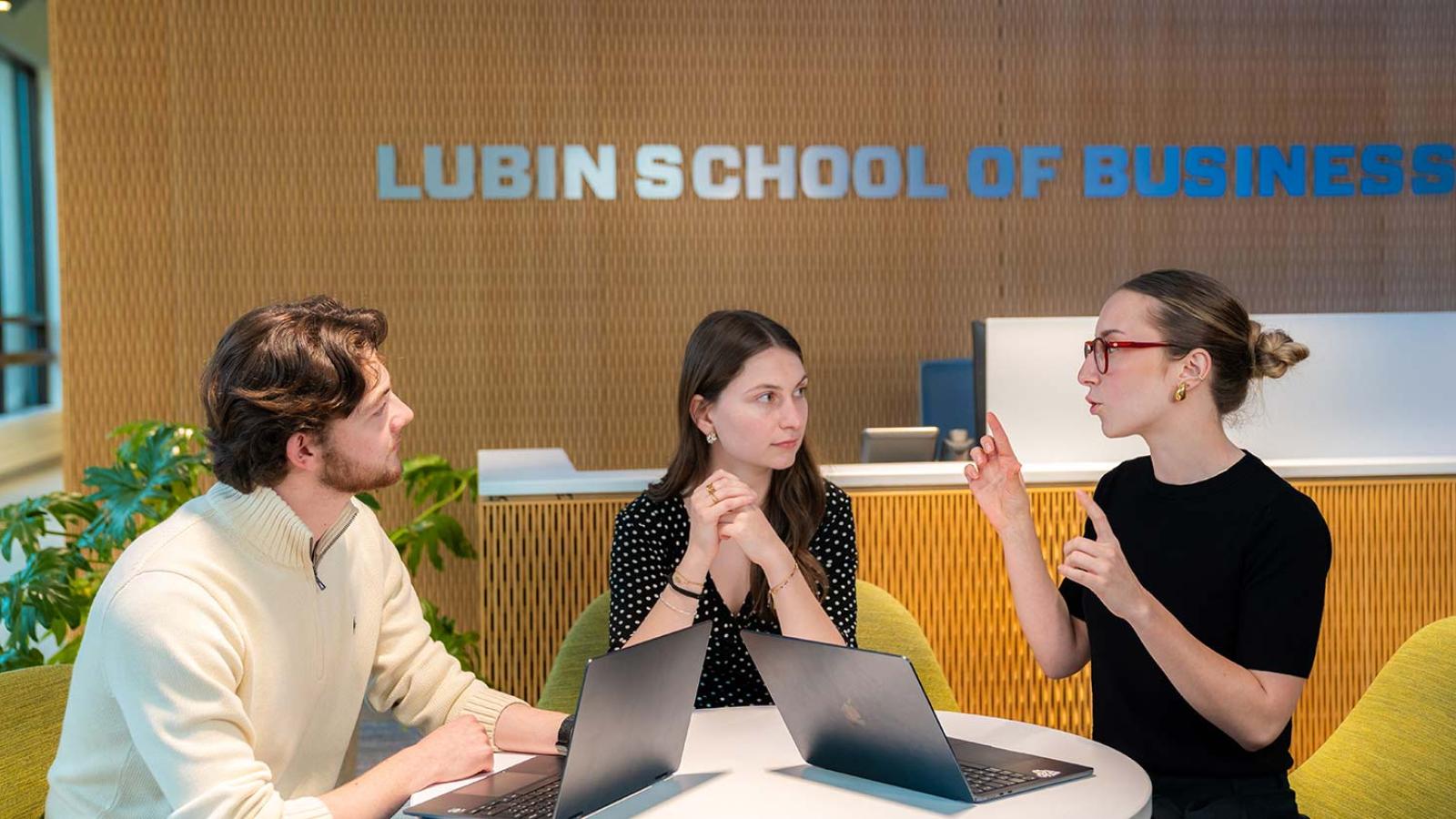 Three Pace University Lubin School of Business students speaking together with laptops open