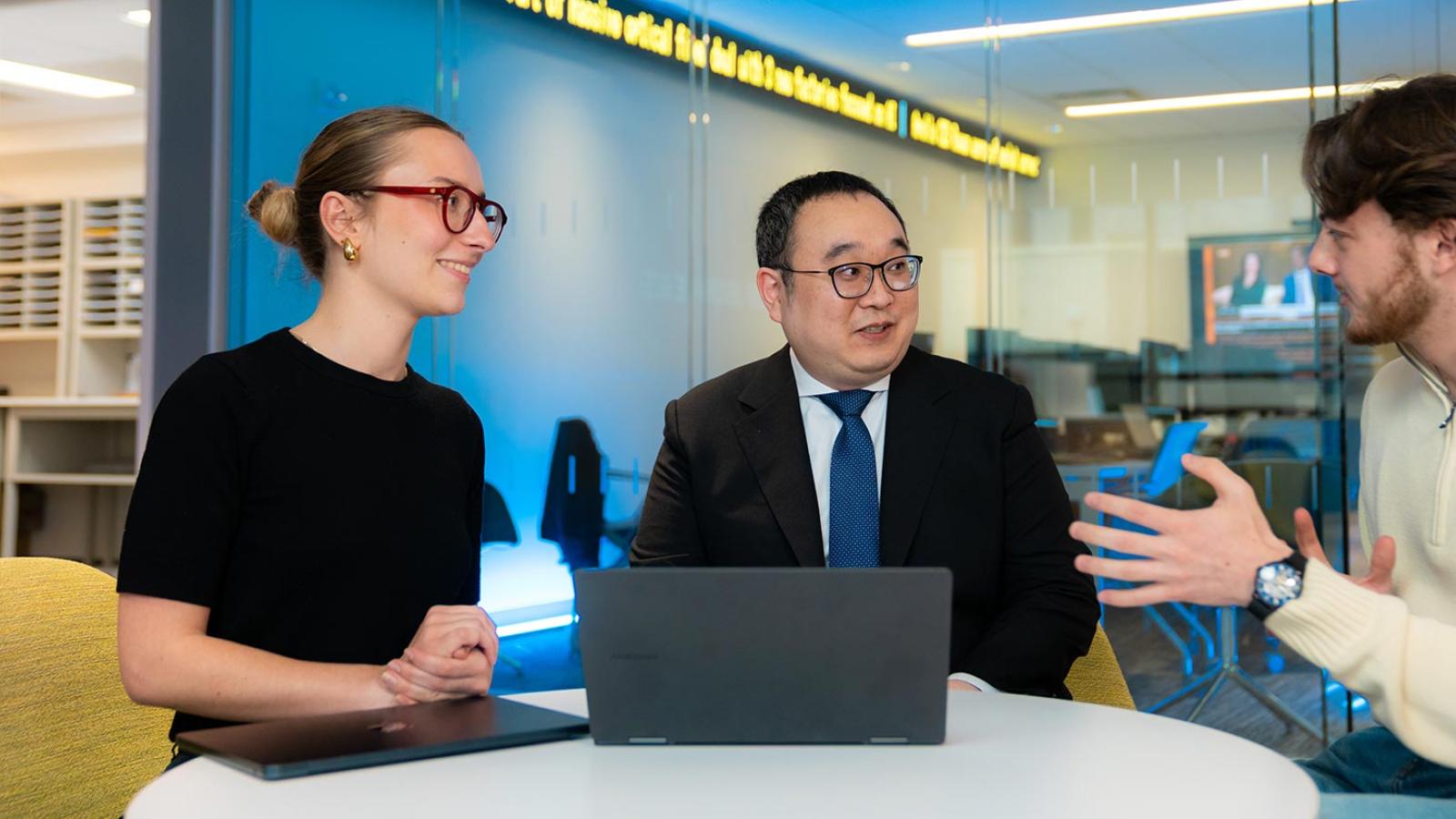 Three Pace University Lubin School of Business students and faculty speaking together at a laptop