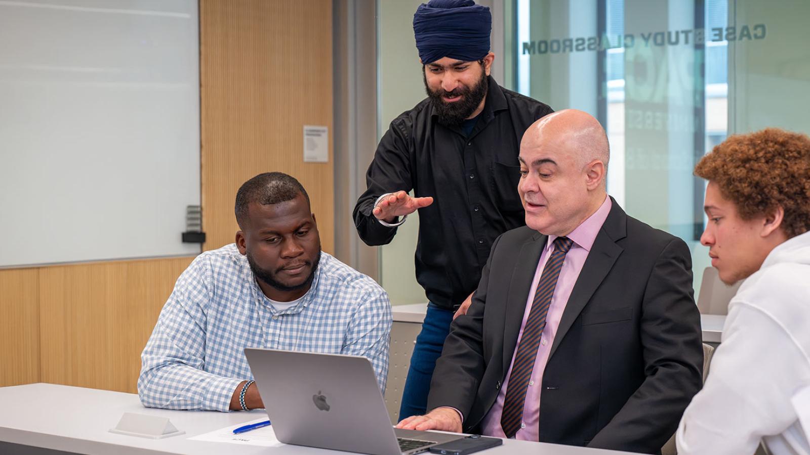 Lubin School of Business students and faculty member looking at laptop together
