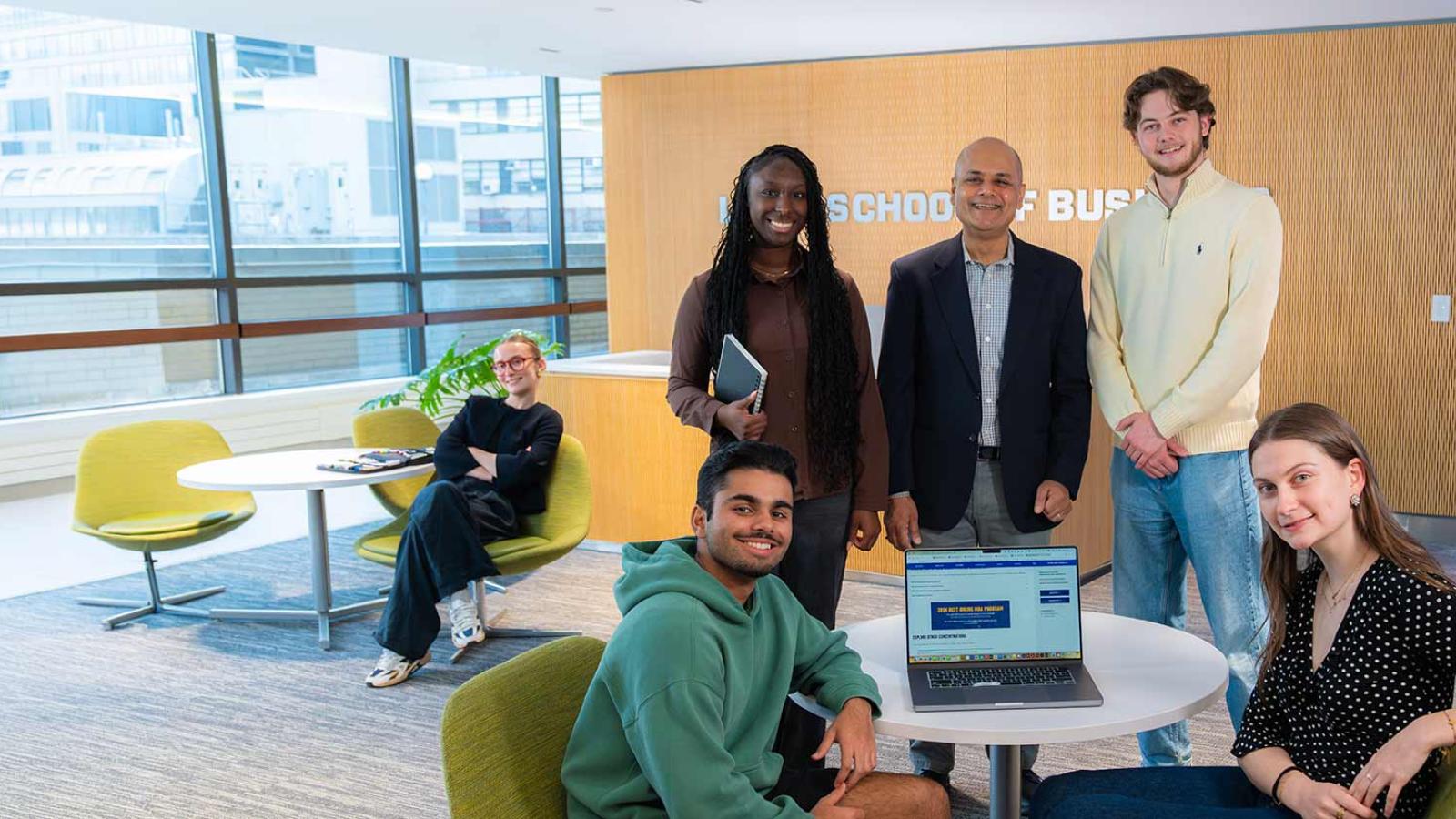 Group of Pace University Lubin School of Business students standing together around a laptop on a table