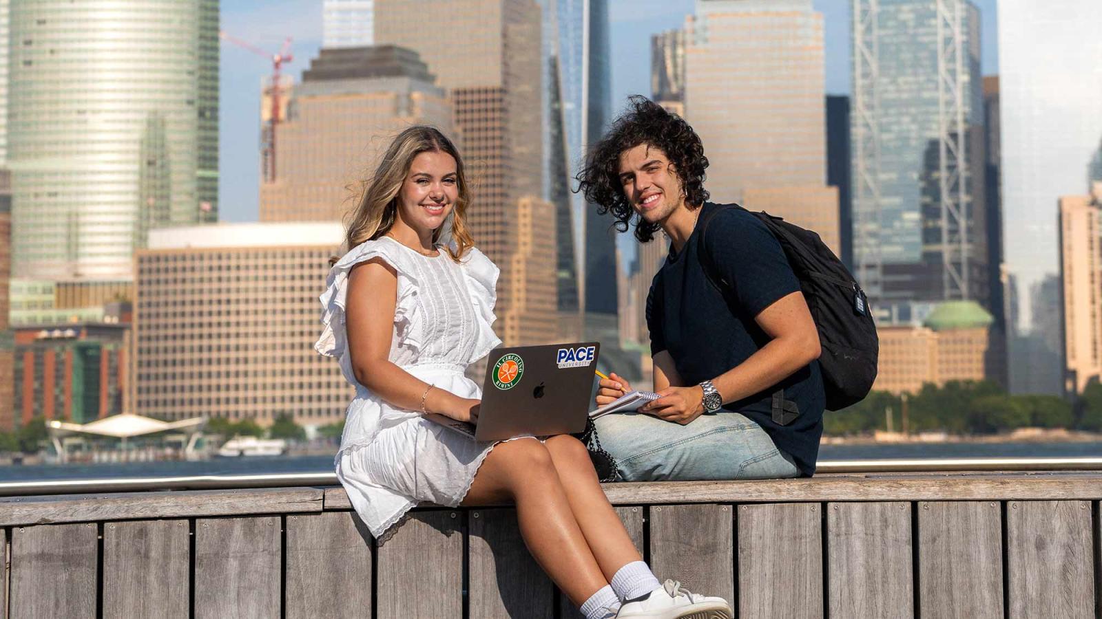 Two Pace University students sitting together, New York buildings behind them