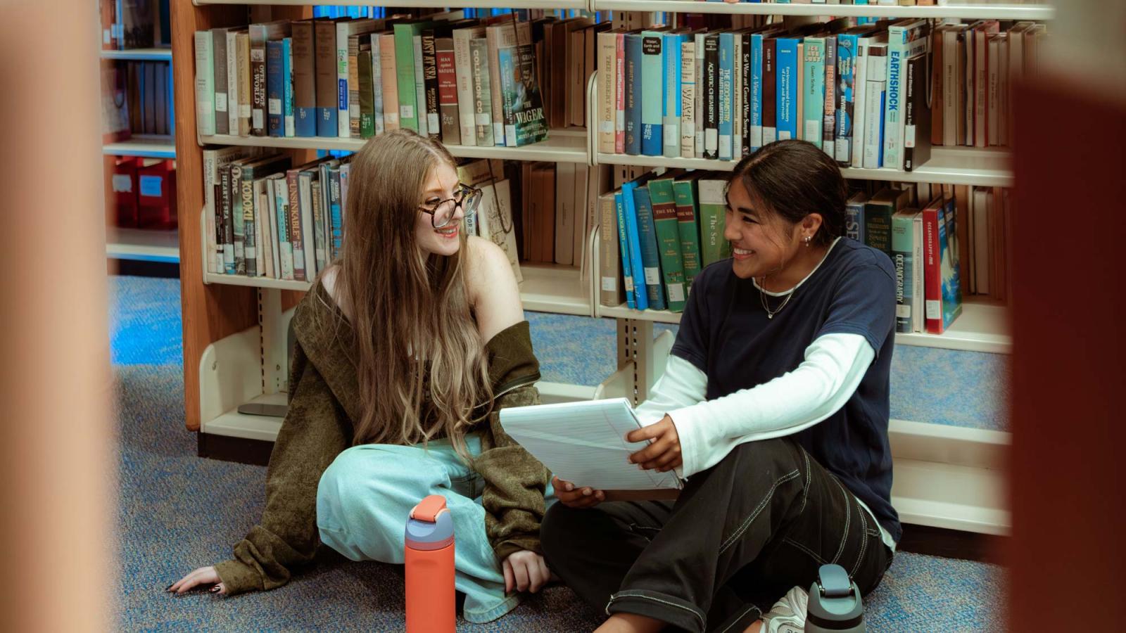 Two Pace University students sitting on the floor in the library, studying.