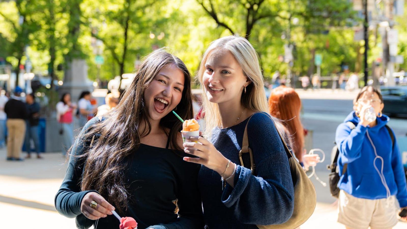 Two Pace University student smiling at the camera, eating an ice cream.