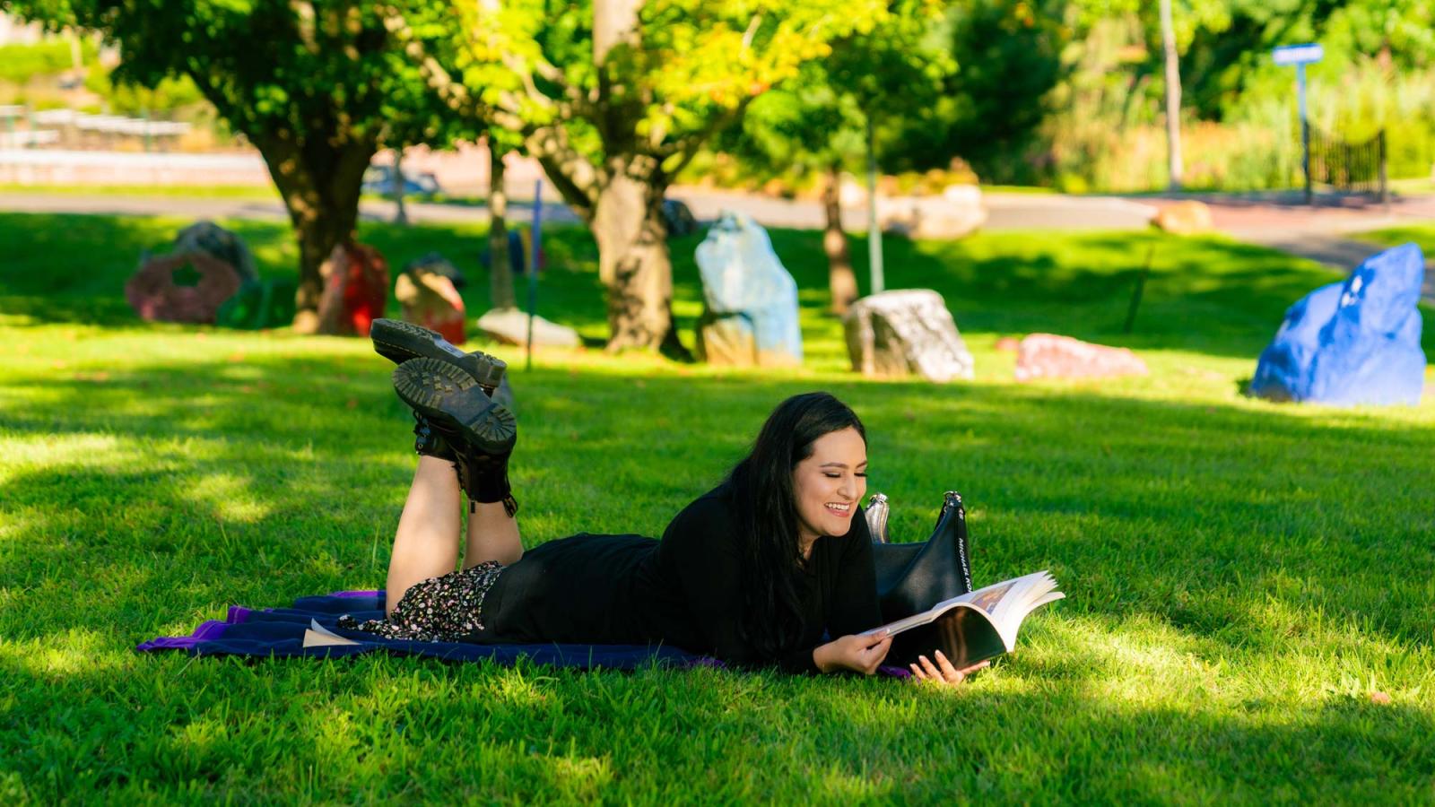 Pace University student laying on the lawn, studying.