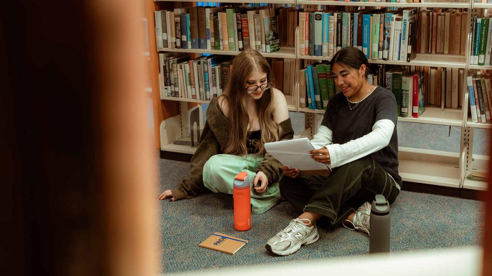 Two Pace University student sitting on the floor in the library, studying.