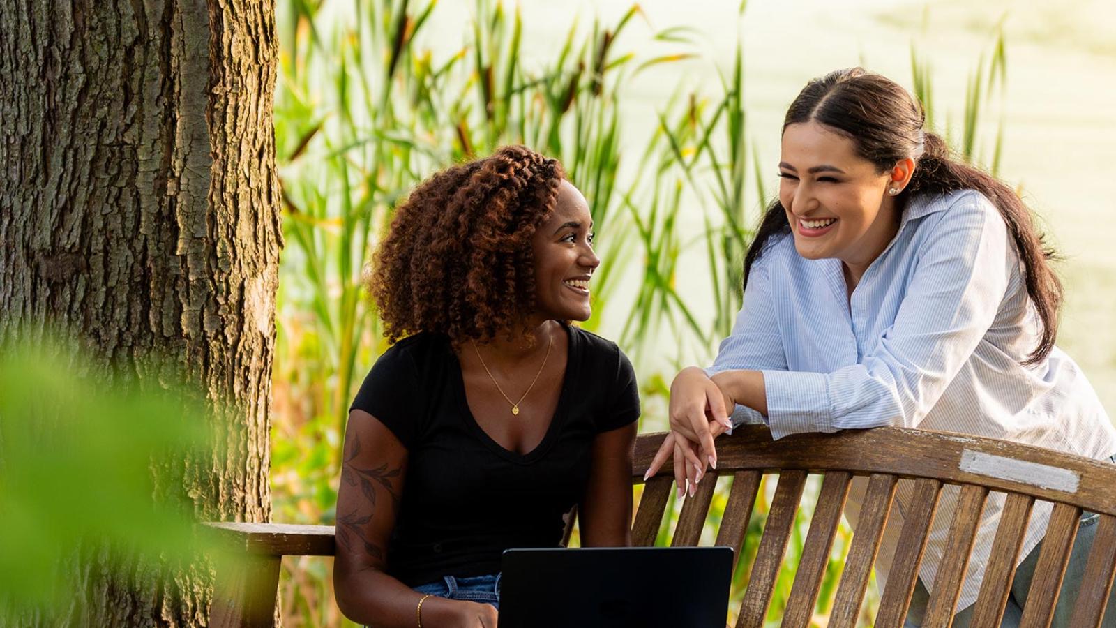 Two Pace University students sitting on a bench, talking on the Westchester campus.