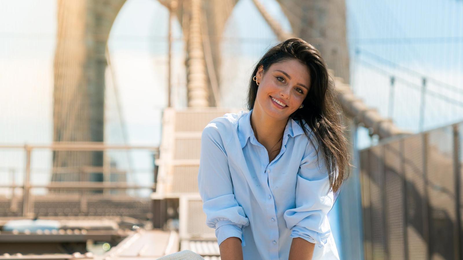 Pace University student sitting on the Brooklyn Bridge, smiling at the camera.
