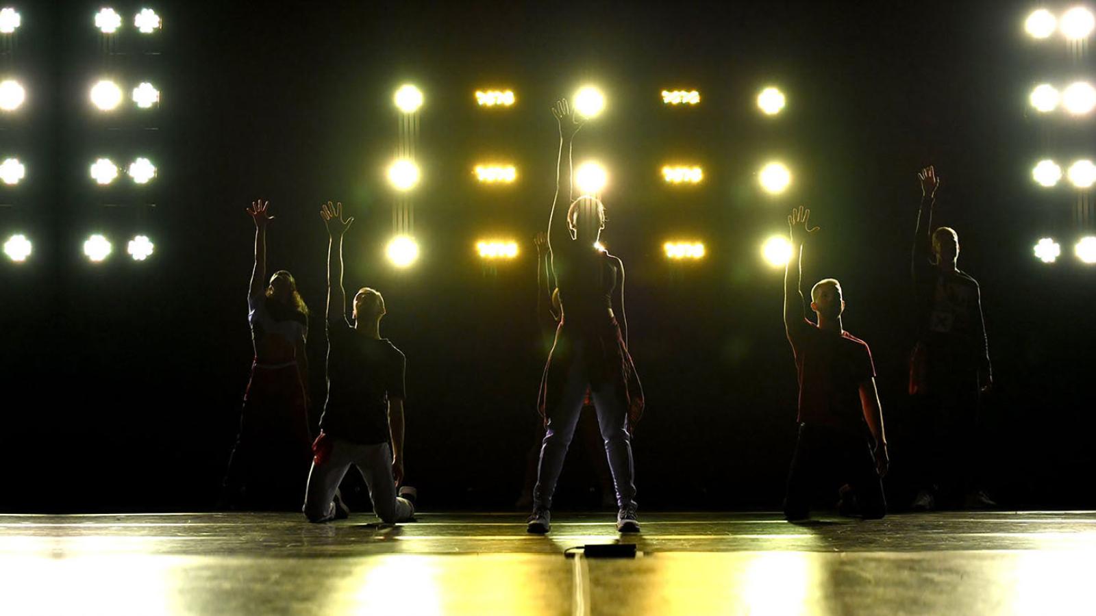 Silhouettes of Pace University students on stage in front of yellow lighting