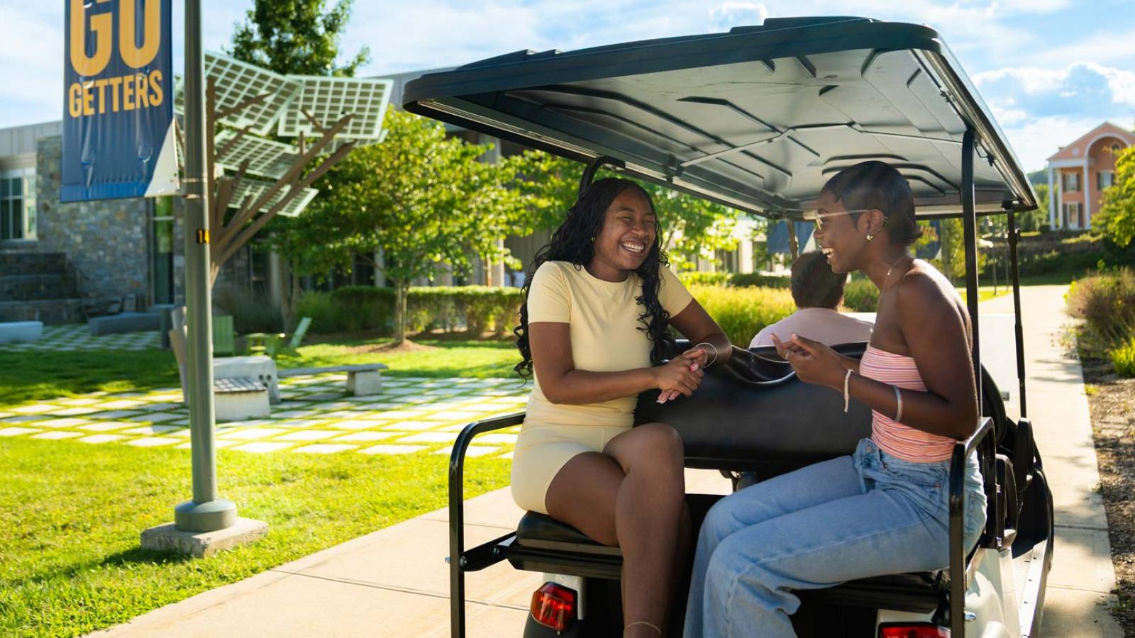 Group of Pace University student riding in a golf cart around the Westchester campus.
