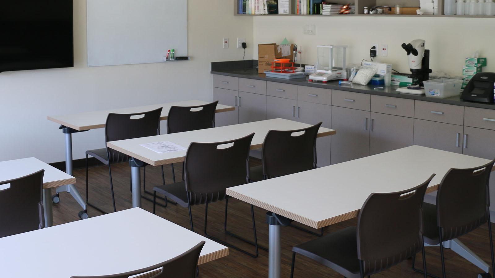 Desks with two chairs each in a labortory and a television at the head of the room