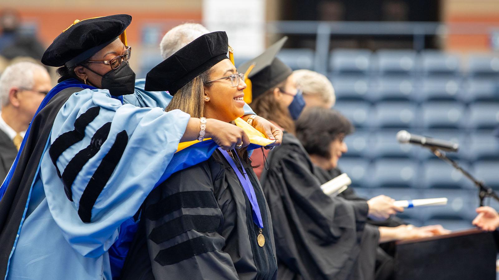 Dean Tresmaine R. Grimes, PhD, places a hood on a Dyson College doctoral candidate.