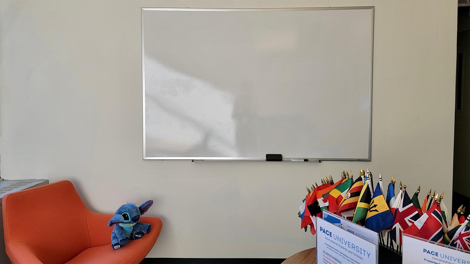 room with an orange chair and stuffed animal, a whiteboard on the wall, and a small table with a miniature world flag display.